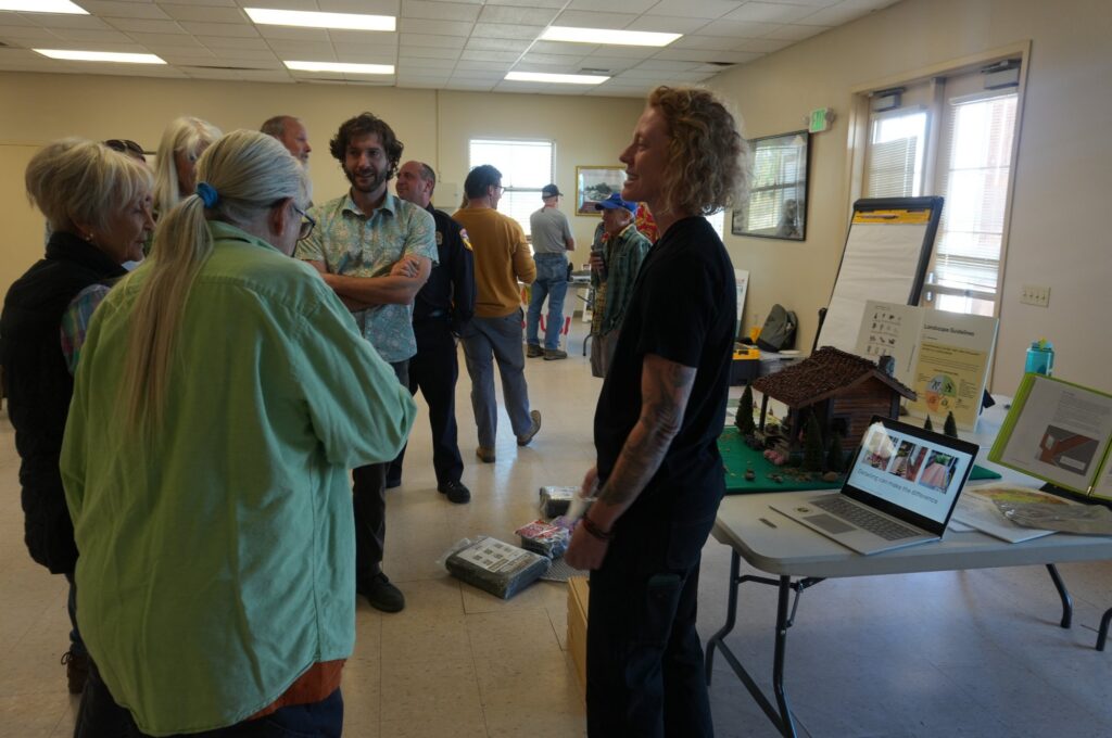 Workshop participants talk around a scale-model home used to demonstrate defensible space and home hardening