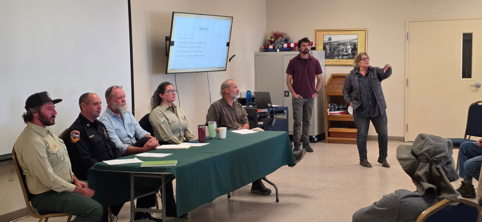 Five wildfire experts seated at a panel table at the Lee Vining Community Center while a facilitator addresses the audience
